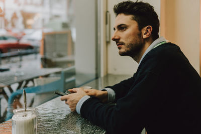 Side view of young businessman sitting by window at cafe