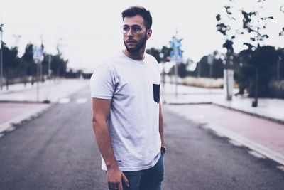 Portrait of young man standing on road against sky