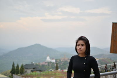 Thoughtful young woman standing on mountain against sky