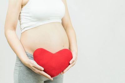 Midsection of woman making heart shape against white background