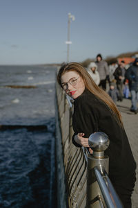 A girl stands on the embankment near the sea, with long red hair, looks at the camera