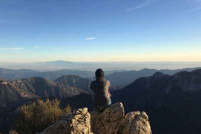 Rear view of young woman sitting on mountain against sky