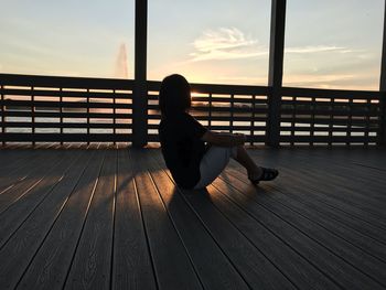 Full length of woman sitting on hardwood floor against sky during sunset