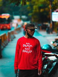 Young man looking away while standing on street in city