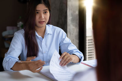 Young woman holding paper while sitting on table