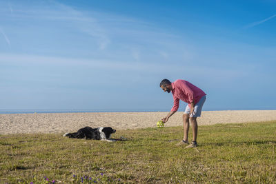 Bearded man playing with dog at beach in sunny day