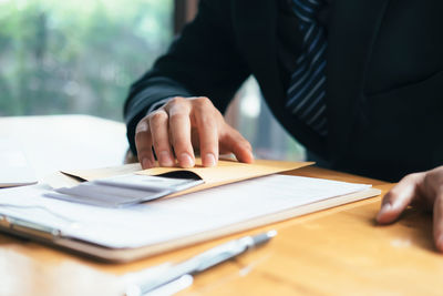 Midsection of man holding envelope with paper currency at table