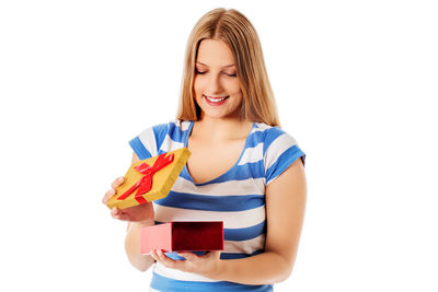 Smiling young woman opening gift against white background