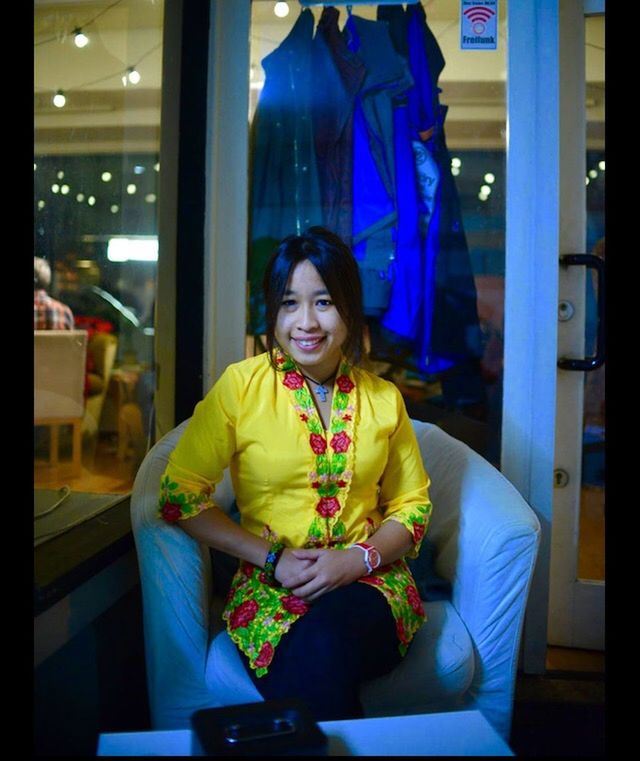 PORTRAIT OF A SMILING YOUNG WOMAN SITTING ON SOFA