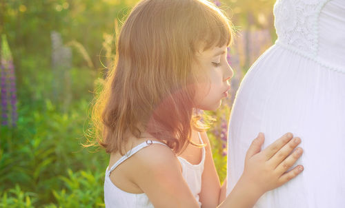 Cute girl kissing belly of pregnant woman