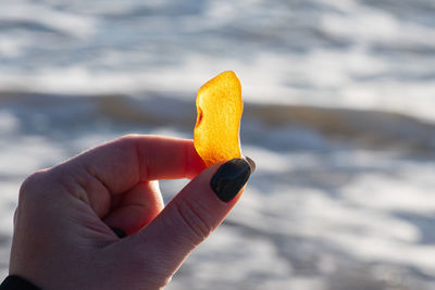 Beautiful big piece of yellow amber in the hand of a girl with water and sea waves on the background