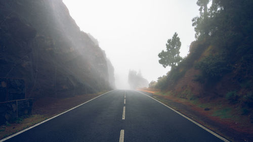 Empty road amidst trees against sky