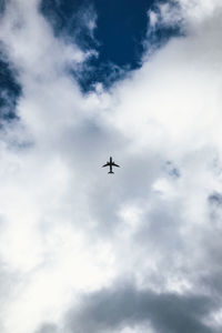 Low angle view of airplane flying against cloudy sky