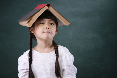 Close-up portrait of girl with book on head against blackboard