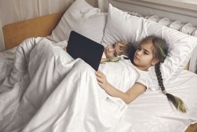 Two siblings watching video in their mobile device in the bed, gadget dependence and addiction