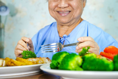 Midsection of smiling senior female patient having food at hospital