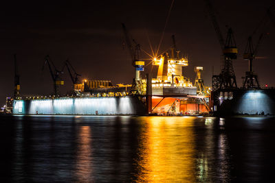 Cranes at illuminated harbor against sky during night