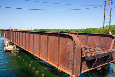 Rusty metallic bridge over river against clear blue sky