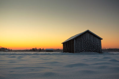 Barn on snow covered field against sky during sunrise
