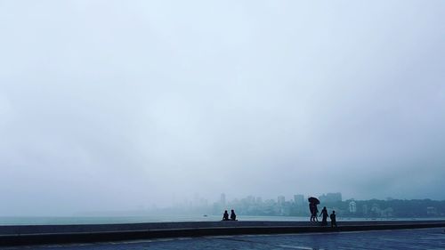 People on footpath by sea against sky in city