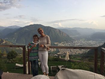Portrait of smiling woman and son holding drinks while standing against mountain range