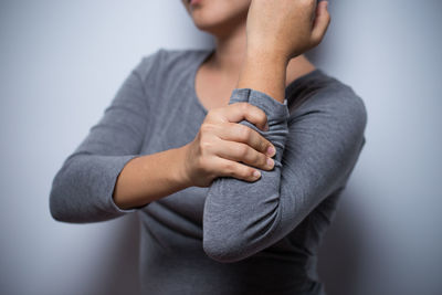 Midsection of woman suffering wrist pain against gray background