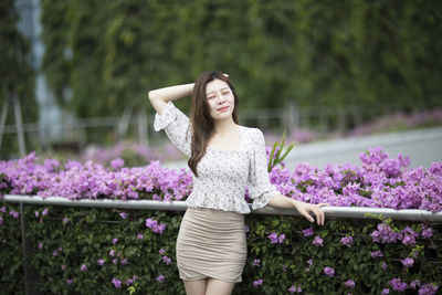 Portrait of young woman standing by flowers at park