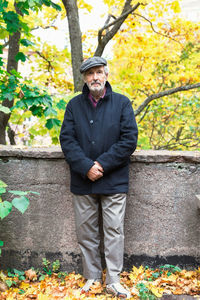 Full length portrait of senior man standing with hands clasped in park during autumn