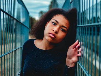 Portrait of young woman standing by metal fence