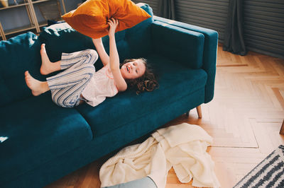 High angle view of girl with cushion lying on sofa at home