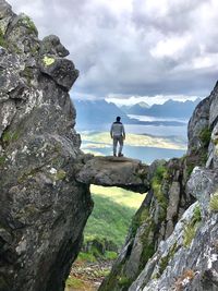 Rear view of man standing on cliff by sea against sky