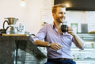 Smiling handsome man holding coffee cup while looking away in cafe