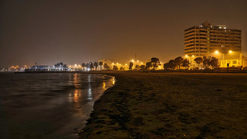 City street by sea against sky at night