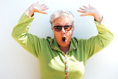 Retired woman with gray short hair with surprised face and raised arms on a white background