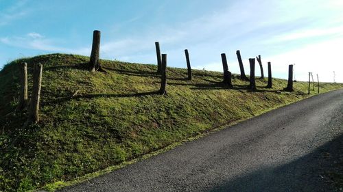 Road by fence on field against sky