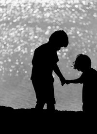 Silhouette sibling holding hands at beach