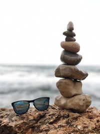 Stack of stones by sunglasses at beach against clear sky