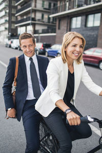 Smiling business people riding on bicycle in city street