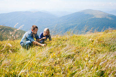 Couple crouching on grass against mountain