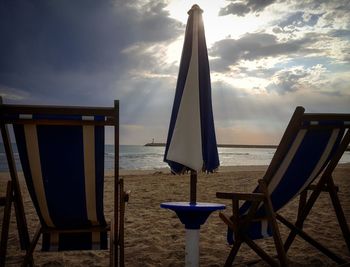 Chairs and tables on beach against sky during sunset