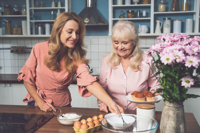 Cheerful daughter and mother preparing muffins at kitchen