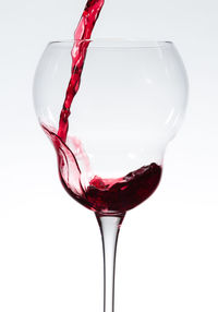 Close-up of wine pouring in wineglass against white background