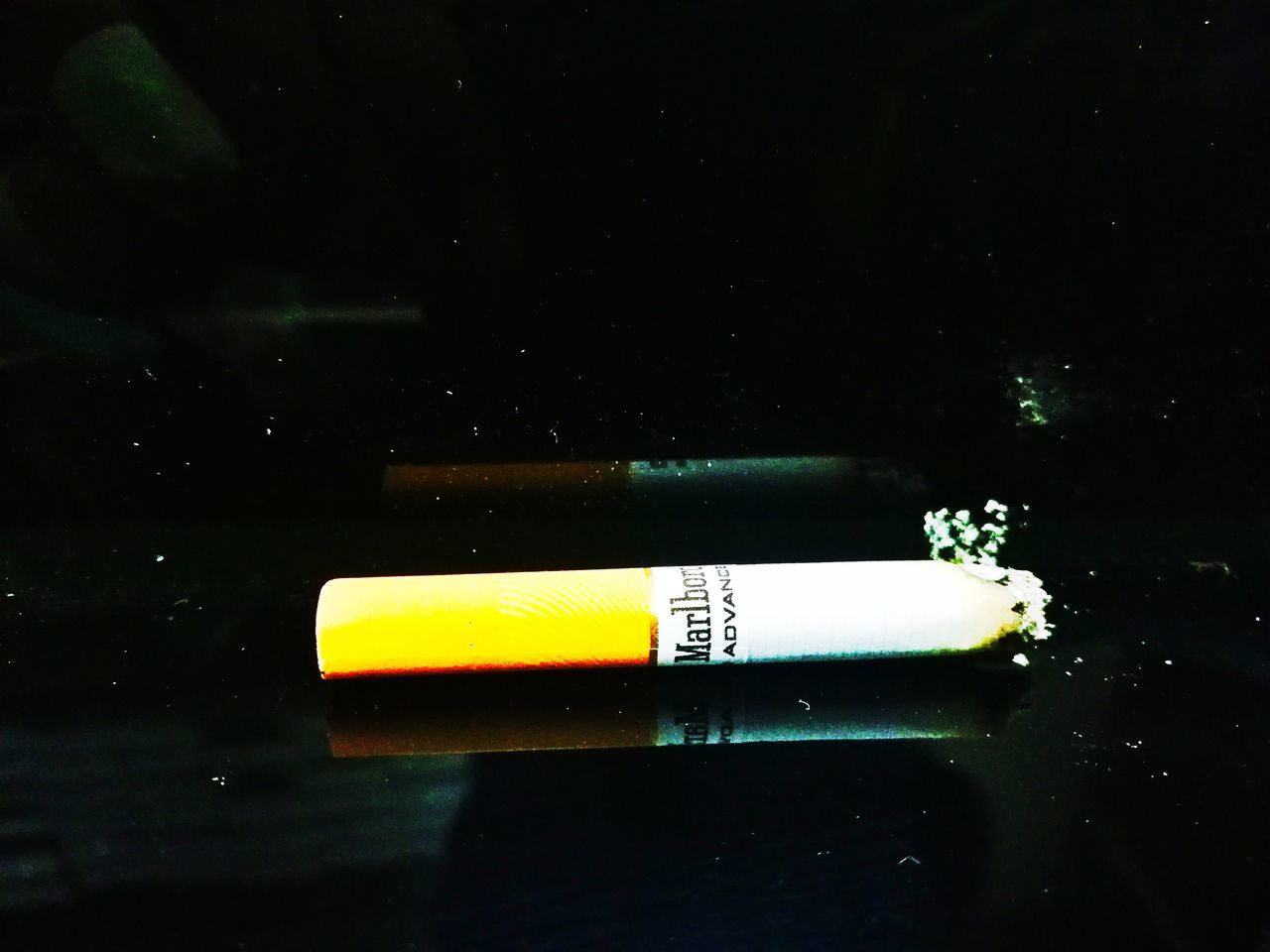 CLOSE-UP OF CIGARETTE SMOKING ON TABLE AGAINST BLACK BACKGROUND