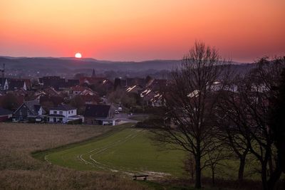 Scenic view of field and buildings against sky during sunset