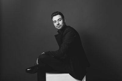 Portrait of young man sitting on chair against gray background