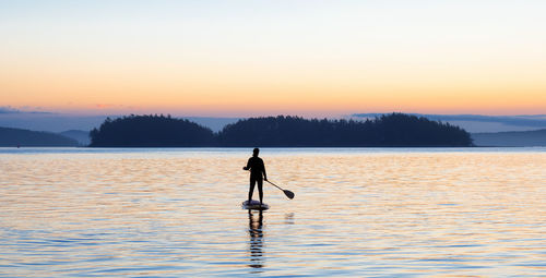 Silhouette man standing in sea against sky during sunset