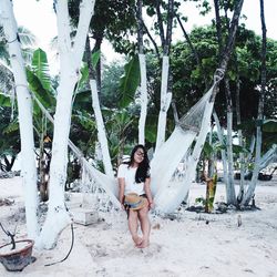 Young woman sitting on hammock amidst trees at beach