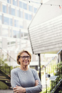 Portrait of smiling businesswoman standing arms crossed at office yard