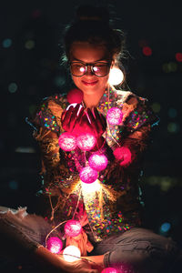 Portrait of young woman standing against illuminated christmas tree