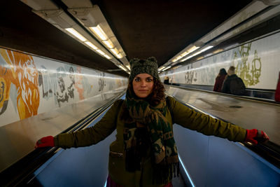 Portrait of woman standing on moving walkway at railroad station